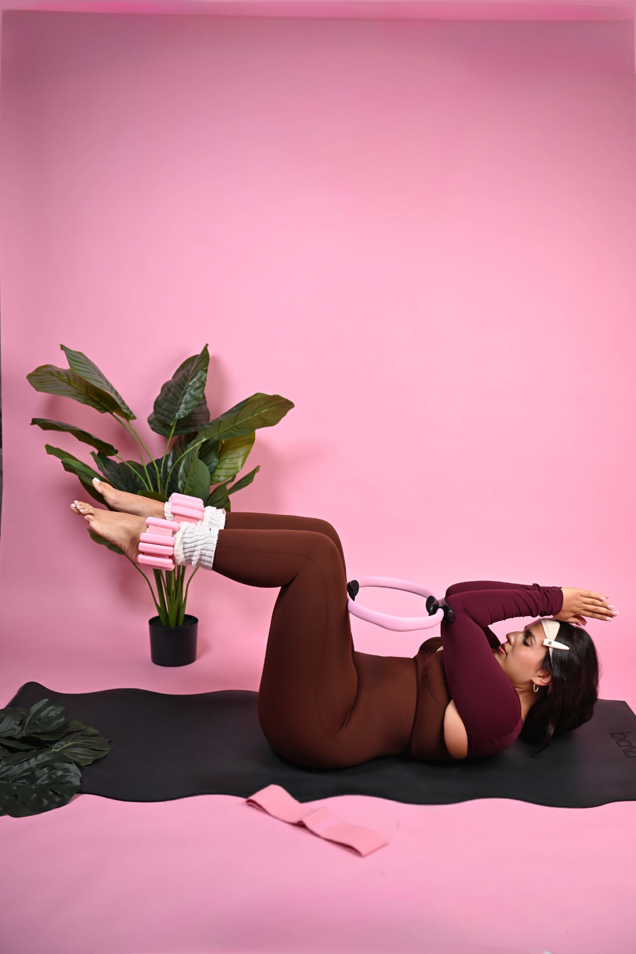 Pilates ring and ankle weights work on a mat against a pink backdrop